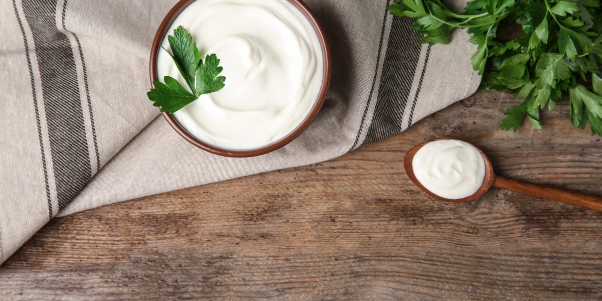 Flat lay composition with sour cream and parsley on wooden table, space for text