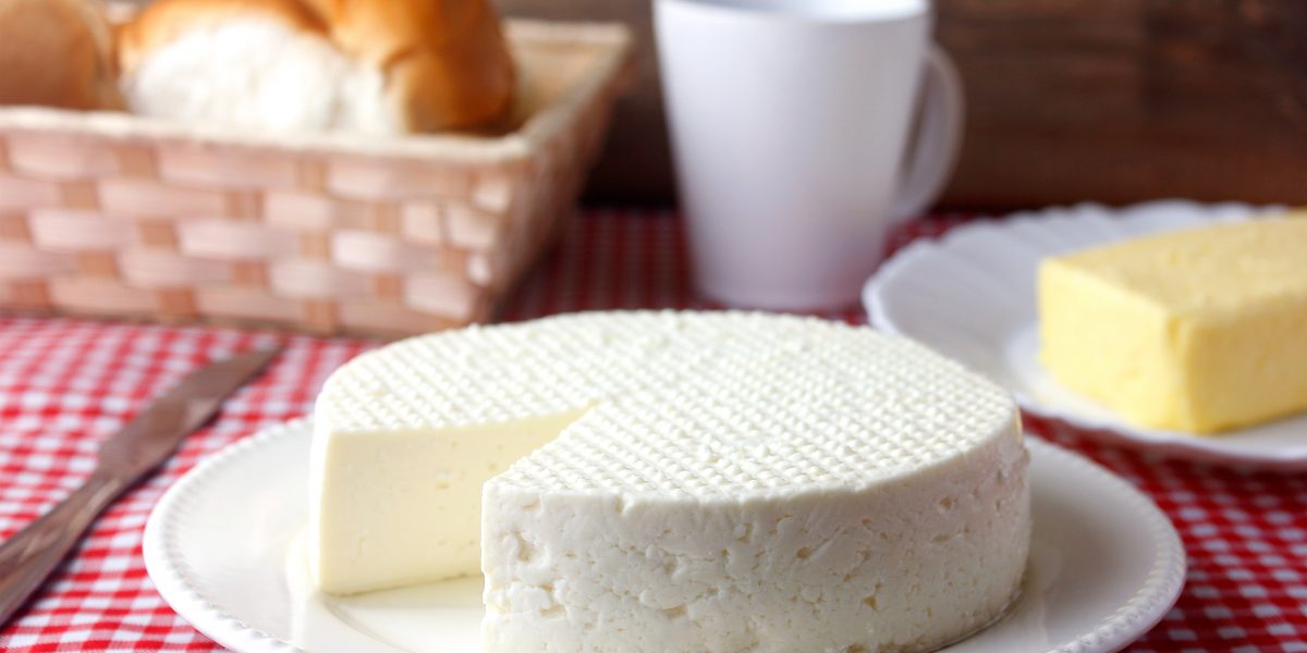 fresh white brazilian minas cheese isolated over wooden board on breakfast table. front view, selective focus